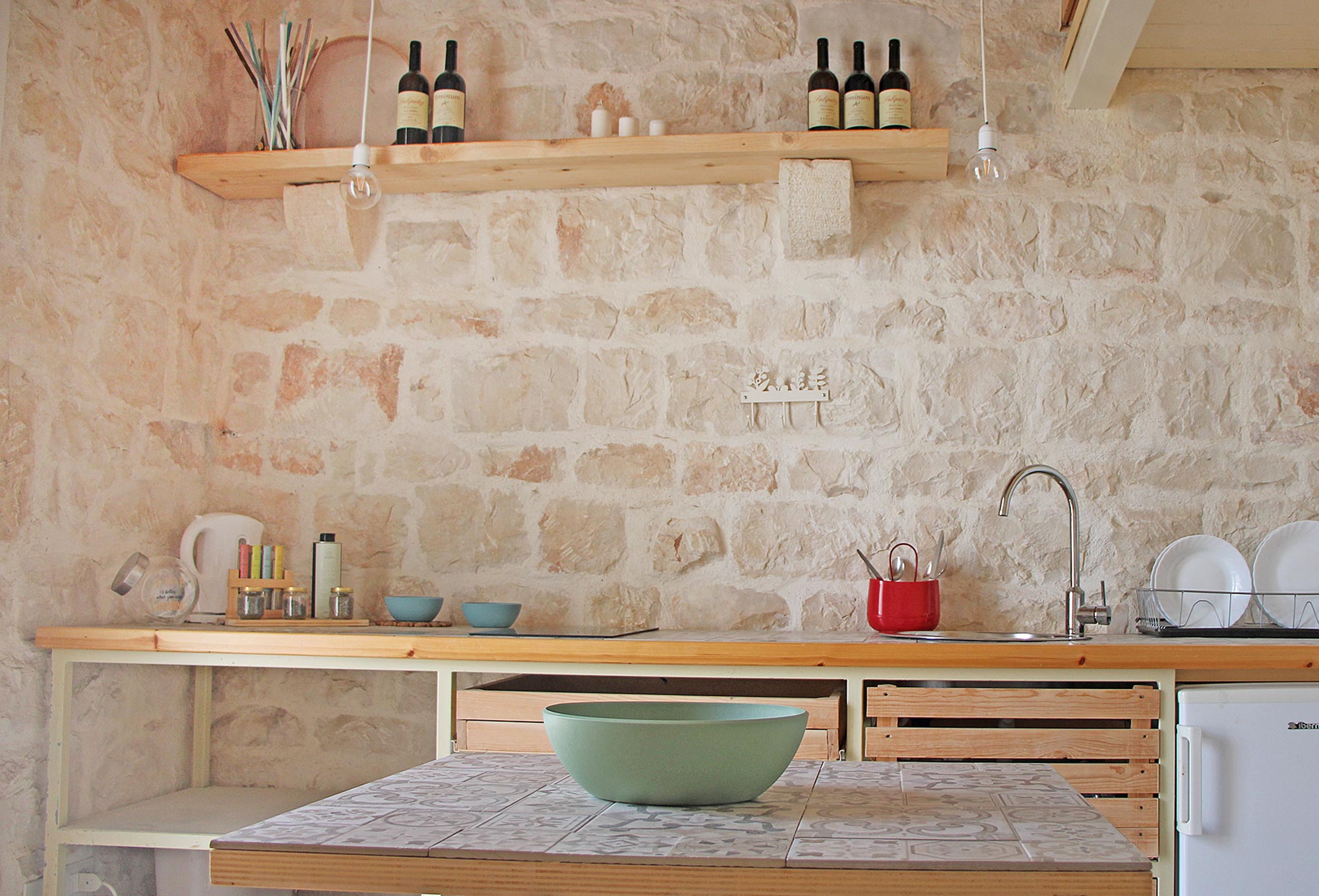 Rustikale Steinküche mit offenem Regal und Weinflaschen im Agriturismo Fondoliva, Sizilien