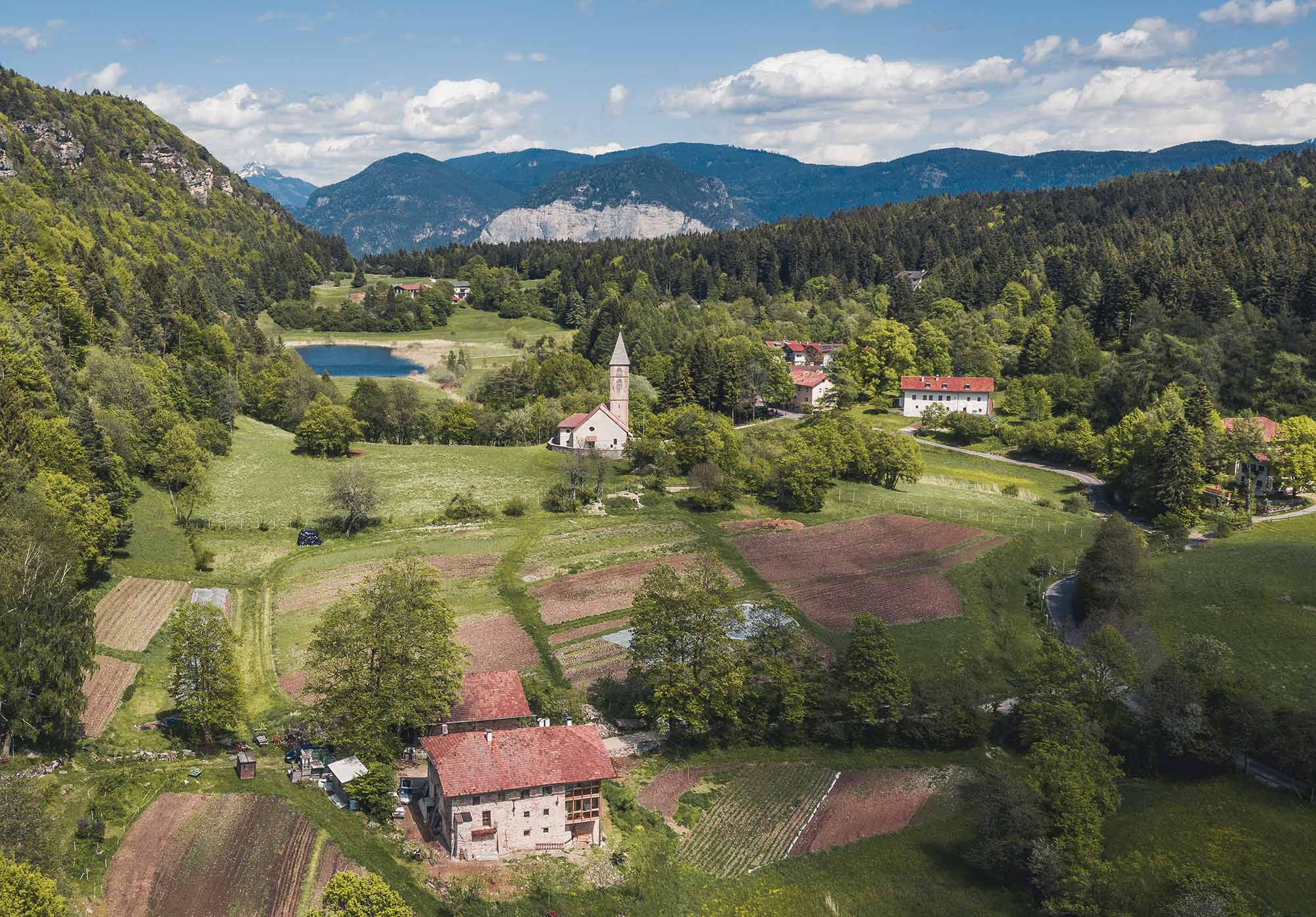 Luftaufnahme des Hofs Unternberg mit Kirche, Feldern und Bergpanorama in Südtirol