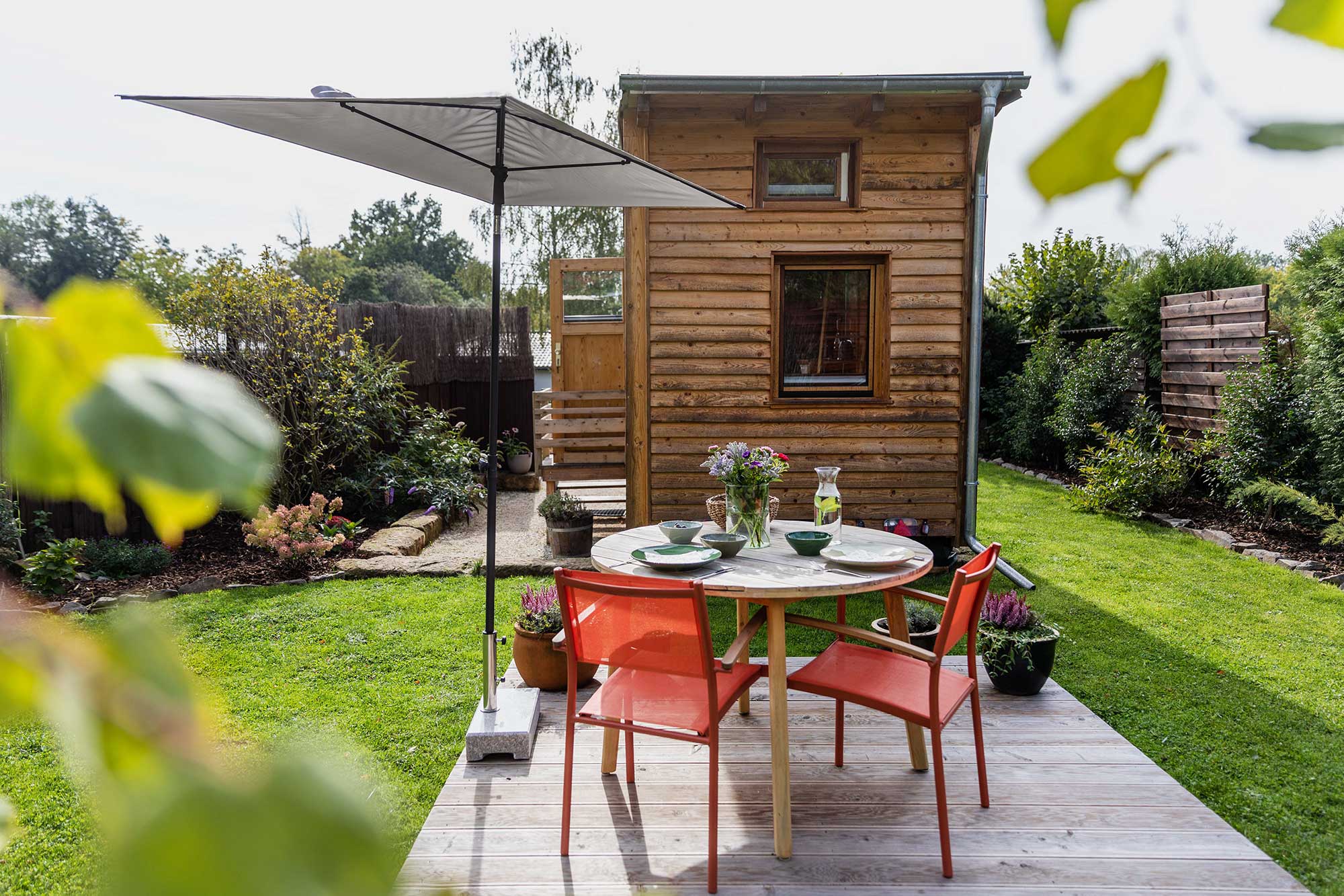 Holzverkleidetes Tiny House Ferienhaus Waldhauszeit mit Sitzplatz, Sonnenschirm und grünem Garten