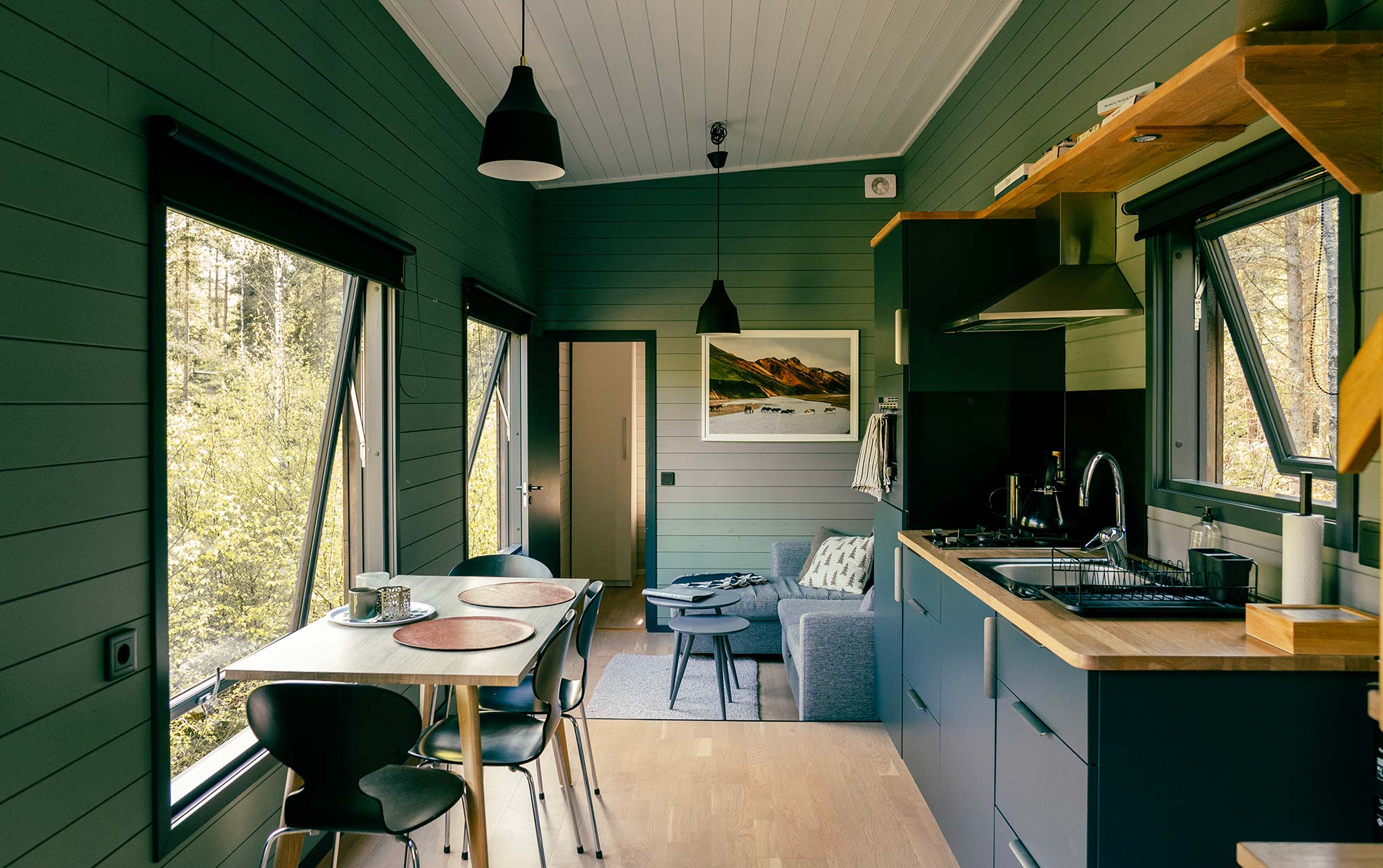 Innenraum der Glamping-Hütte INFOREST mit dunkelgrüner Holzverkleidung, Essbereich, Sofa und offener Küche