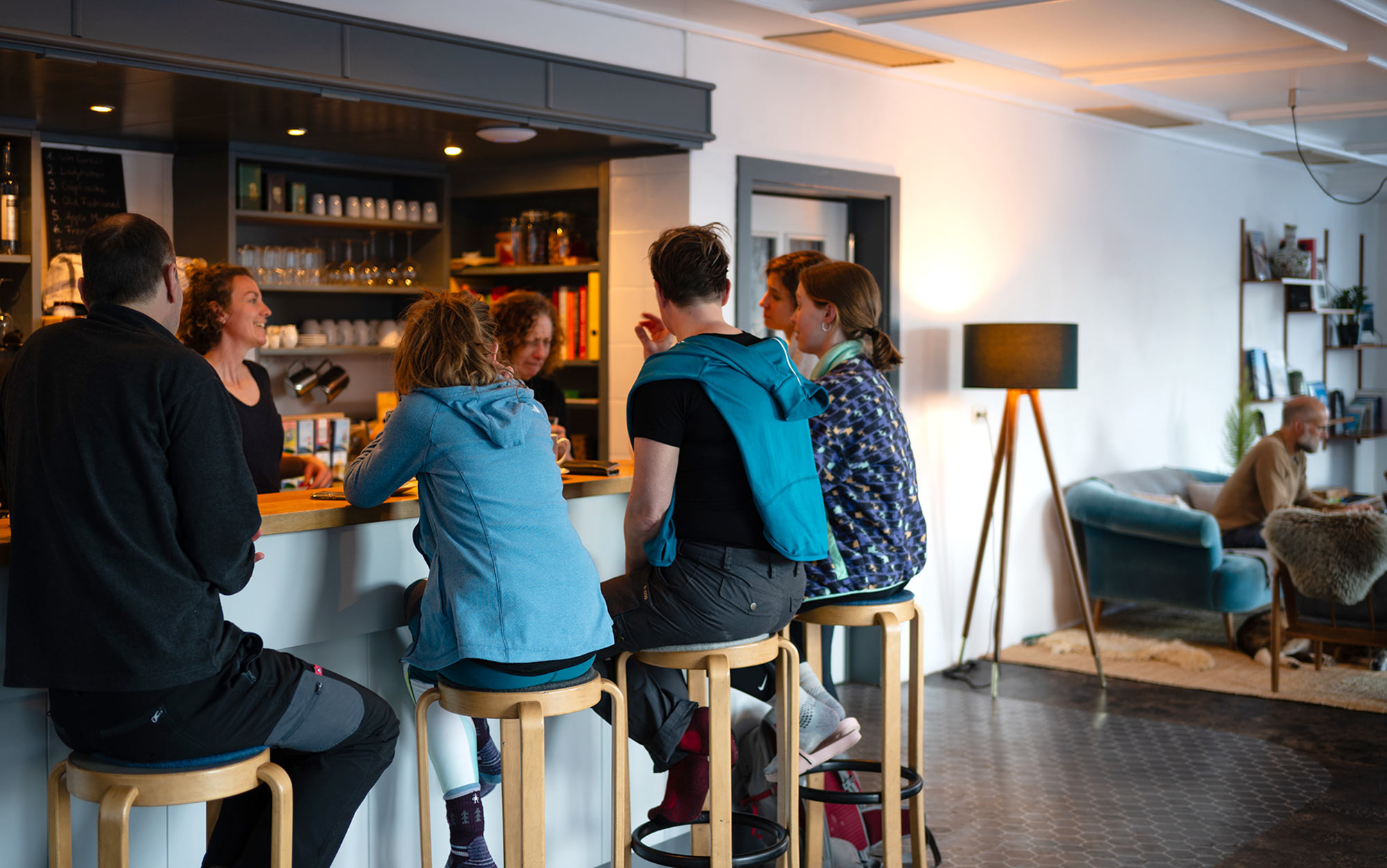 Gäste sitzen an der Bar der MoaAlm Mountain Retreat und unterhalten sich mit dem Team in gemütlicher Lounge-Atmosphäre