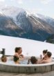 Gäste entspannen gemeinsam im holzbefeuerten Hot Tub der MoaAlm Mountain Retreat mit Blick auf schneebedeckte Berge