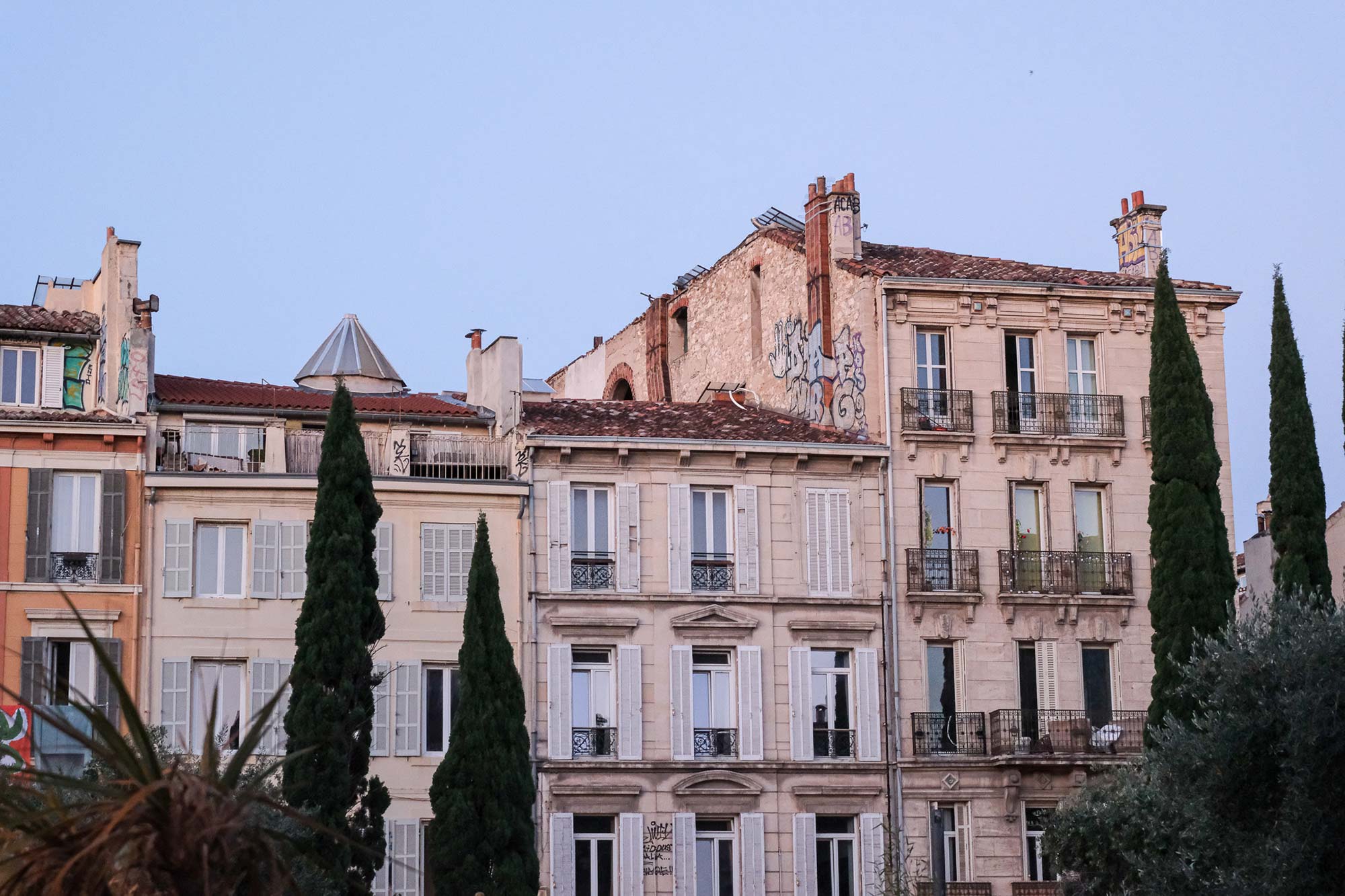 Prächtige Altbaufassaden aus warmem Sandstein mit Fensterläden, schmiedeeisernen Balkonen und Zypressen in Marseille