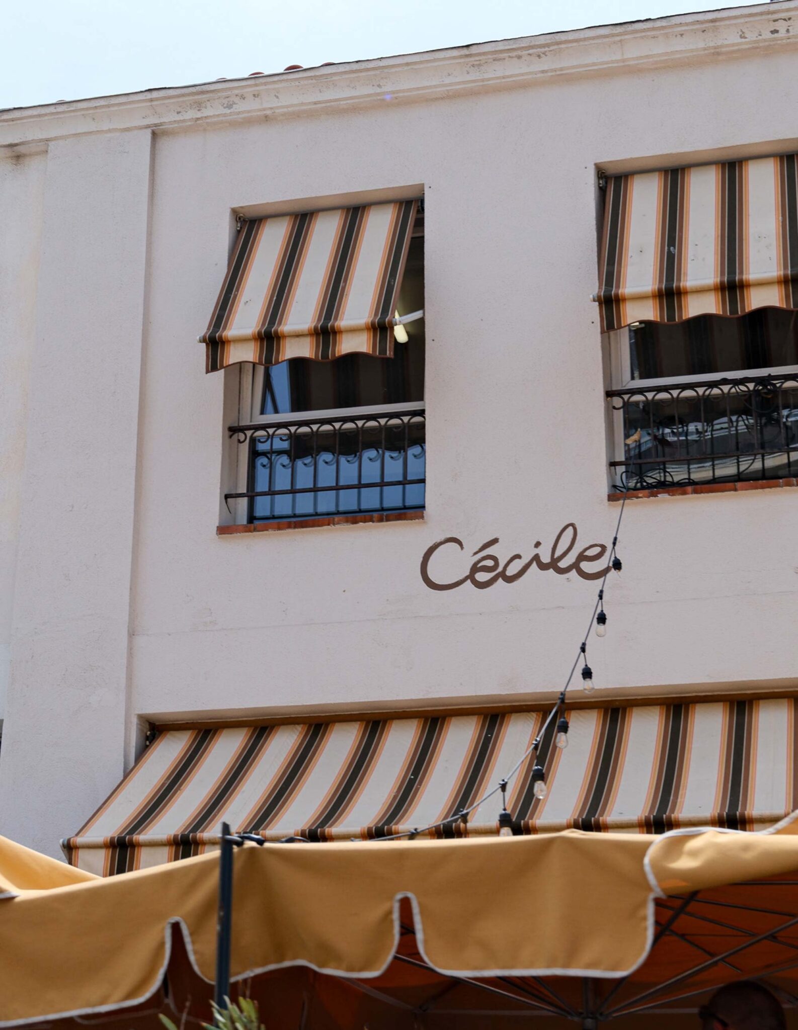 Helle Hausfassade mit gestreiften Markisen, Lichterkette und geschwungenem Schriftzug „Cécile“ des Cécile Food Club in Marseille