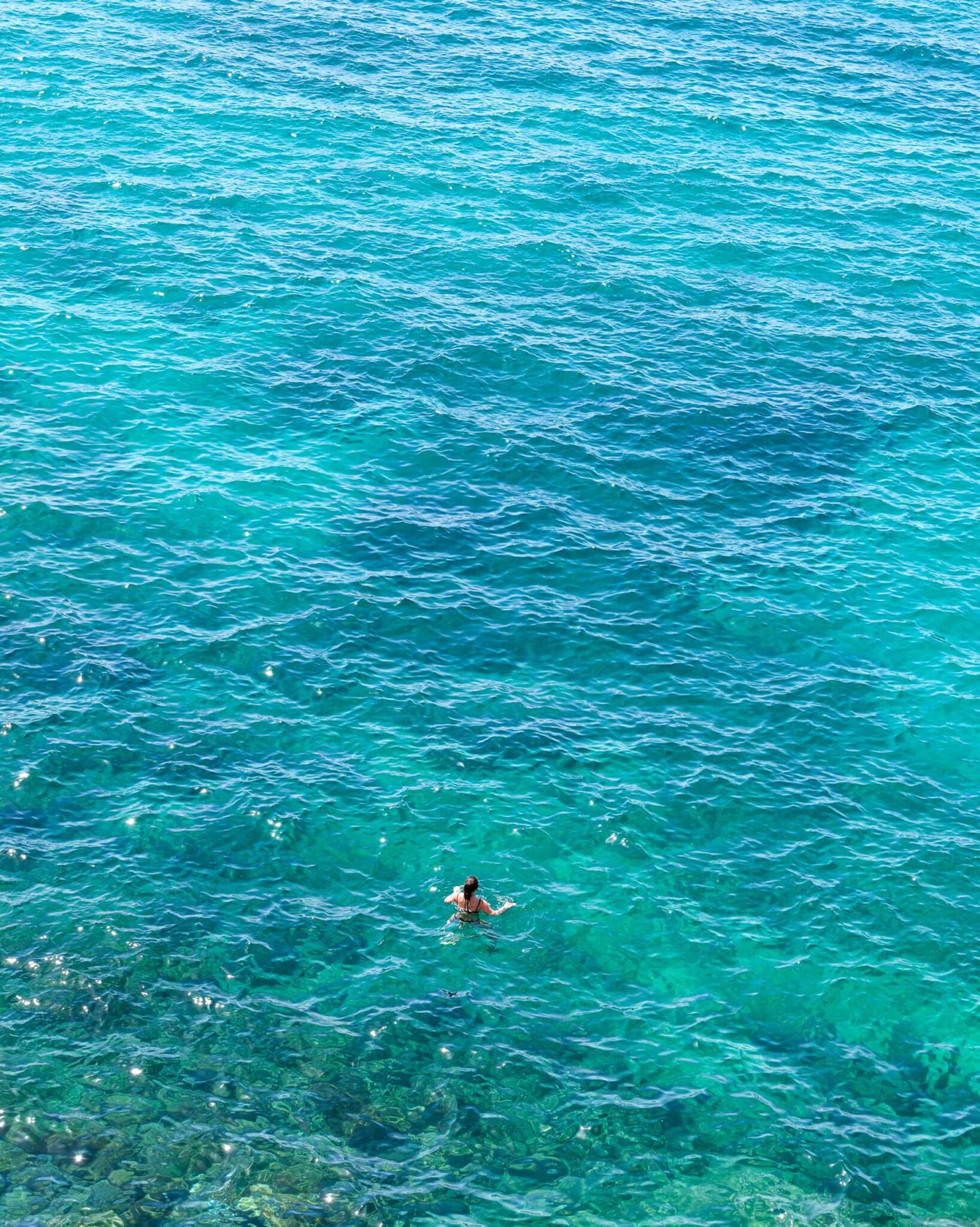 Schwimmerin von oben im klaren, türkisfarbenen Mittelmeer an der Felsküste von Marseille