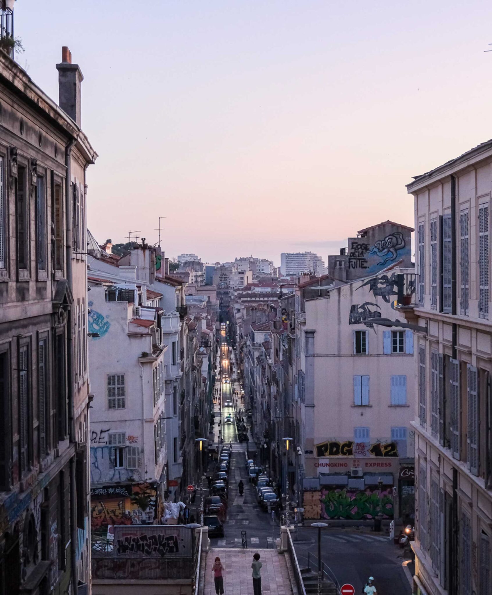 Blick von einer Treppe über eine lange Straße mit Altbauten und Graffiti in Marseille in der rosa Abenddämmerung