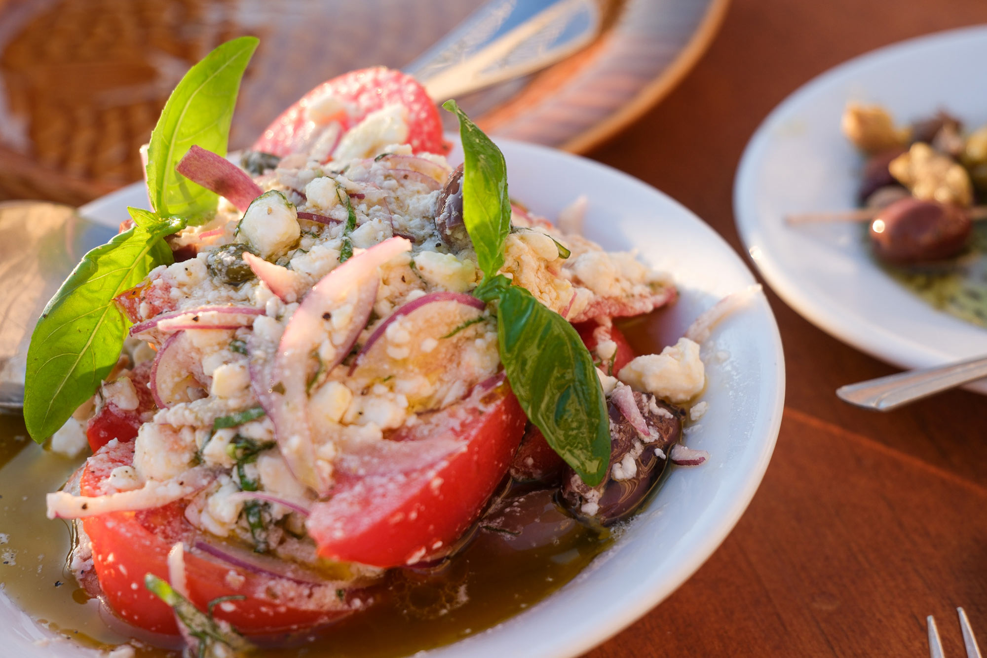 Tomatensalat mit Feta, roten Zwiebeln, Kapern, Oliven und Basilikum im Abendlicht in Marseille
