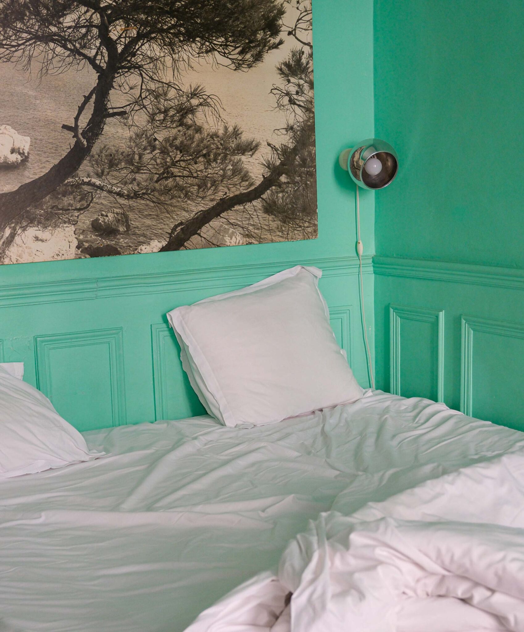Gästezimmer mit mintgrüner Wandvertäfelung, weißer Bettwäsche, Chrom-Wandleuchte und großem Schwarz-Weiß-Foto der Calanques-Küste in der Pension Edelweiss in Marseille