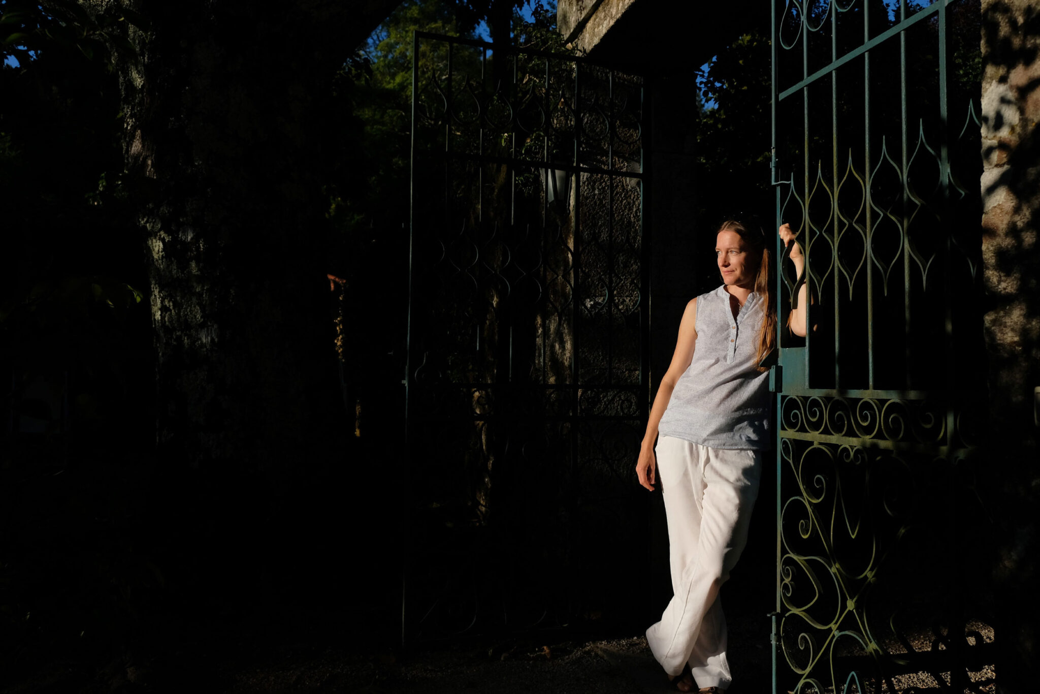 Frau in heller Kleidung lehnt im Abendlicht am schmiedeeisernen Eingangstor der Quinta da Bouça d’Arques