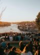 Viele Menschen sitzen bei Sonnenuntergang auf einer Wiese und einer Mauer über dem Douro in Porto, rechts die Altstadt Ribeira, im Hintergrund die Arrábida-Brücke