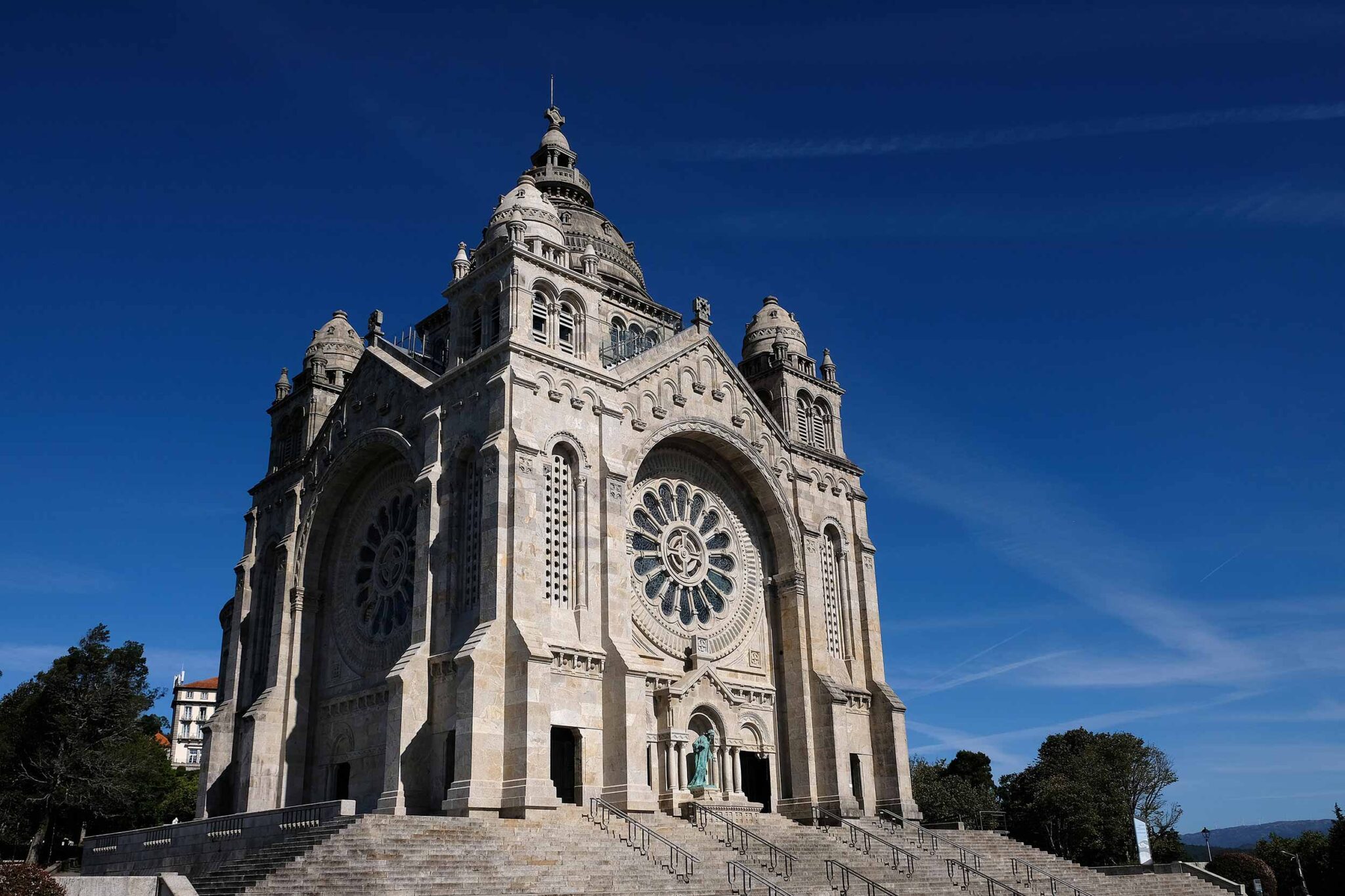 Fassade der Basilika Santa Luzia in Viana do Castelo mit großer Fensterrosette und Freitreppe vor blauem Himmel